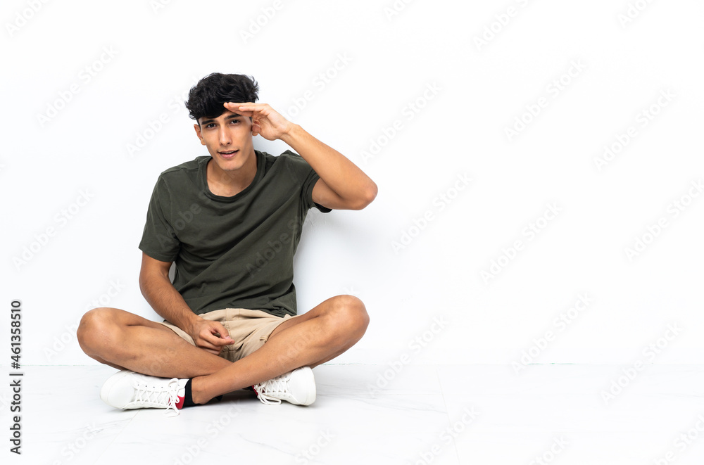 Young Argentinian man sitting on the floor looking far away with hand to look something Young Argentinian man sitting on the floor looking far away with hand to look something