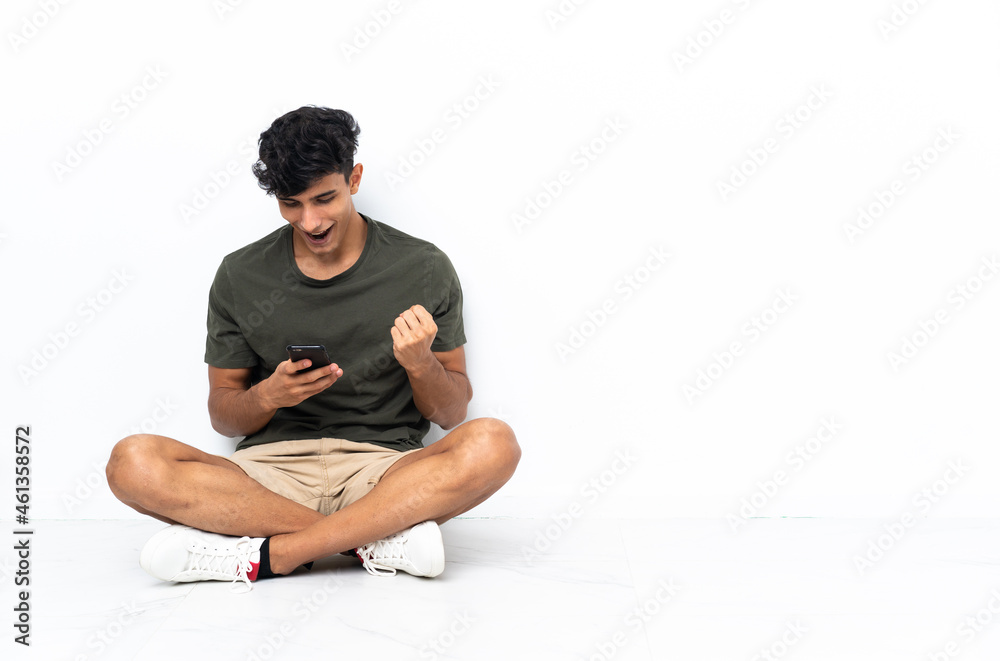 Young Argentinian man sitting on the floor surprised and sending a message Young Argentinian man sitting on the floor surprised and sending a message