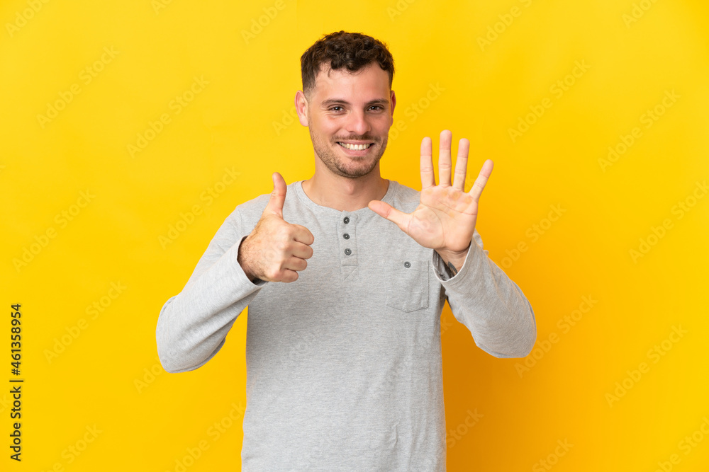 Young caucasian handsome man isolated on yellow background counting six with fingers Young caucasian handsome man isolated on yellow background counting six with fingers