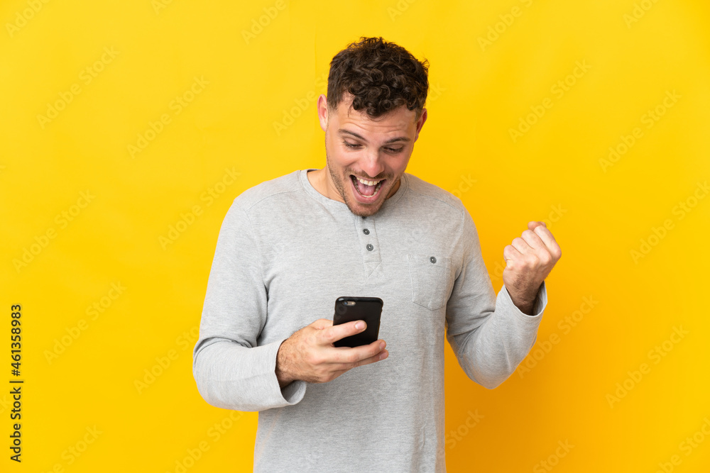 Young caucasian handsome man isolated on yellow background surprised and sending a message Young caucasian handsome man isolated on yellow background surprised and sending a message