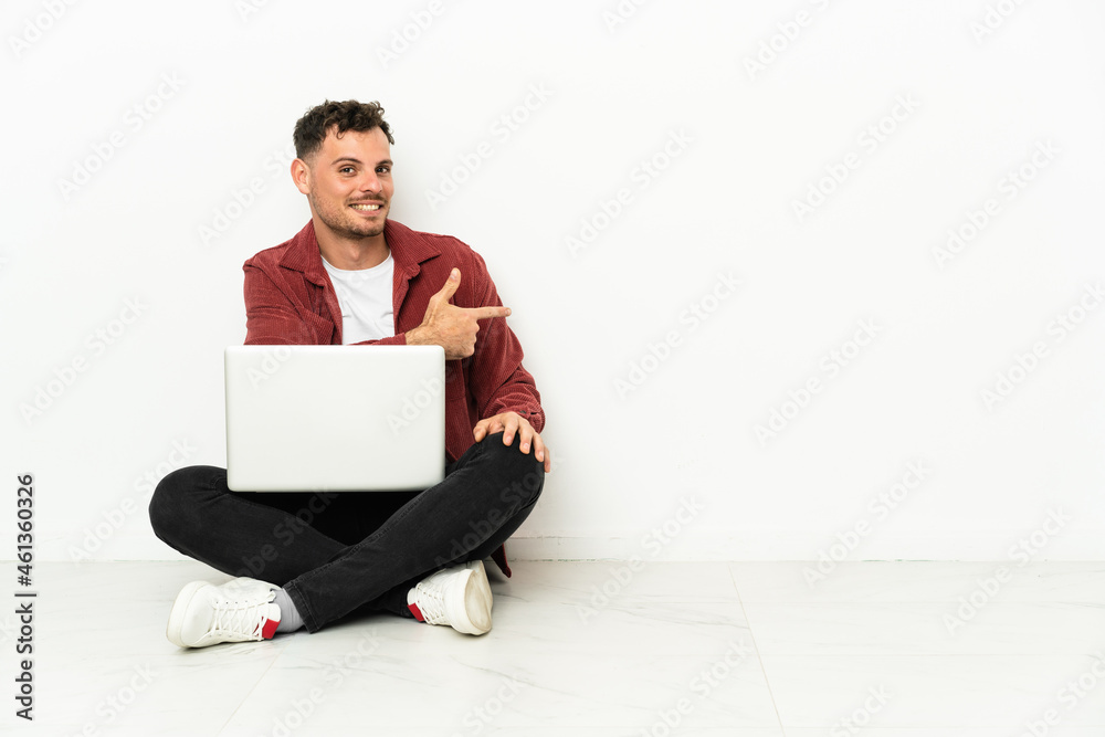 Young handsome caucasian man sit-in on the floor with laptop pointing back Young handsome caucasian man sit-in on the floor with laptop pointing back