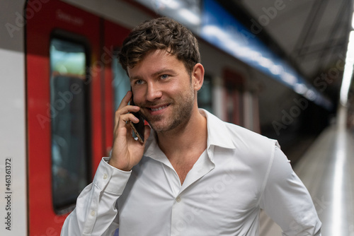 Positive male entrepreneur talking on smartphone near train