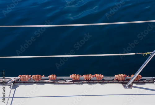 Four sets of fingers hanging onto side of yacht in calm water photo