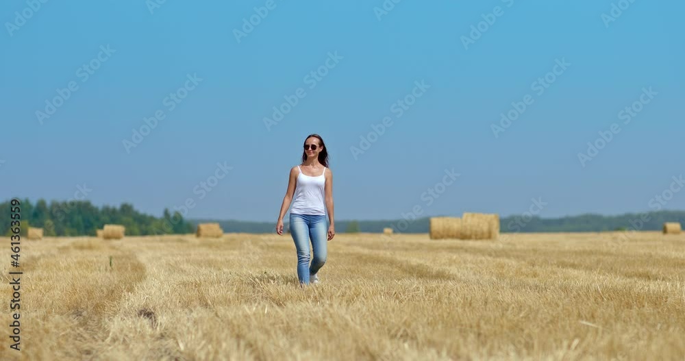 Pretty young woman walks through a mown field and smiles, she is happy. Cute woman walks in a field with haystacks. Beautiful rural landscape, blue sky. 4k, ProRes Pretty young woman walks through a mown field and smiles, she is happy. Cute woman walks in a field with haystacks. Beautiful rural landscape, blue sky. 4k, ProRes