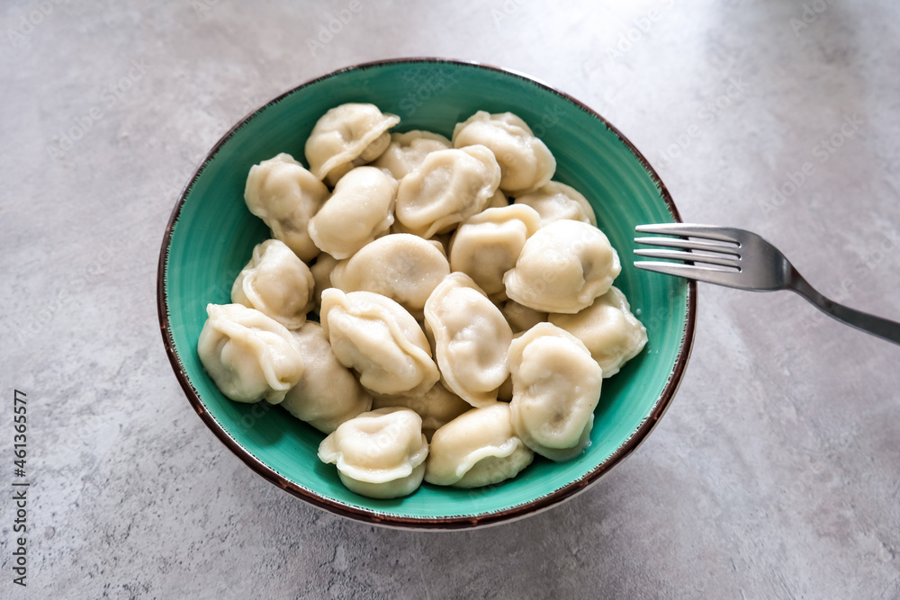 Tasty meat dumplings in green plate with fork on a table, russian pelmeni Tasty meat dumplings in green plate with fork on a table, russian pelmeni