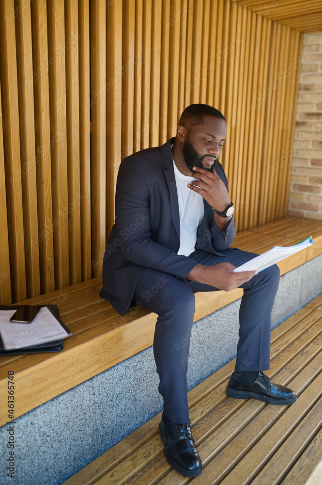A businessman in a suit sitting on a bench with documents for analyzing in hands A businessman in a suit sitting on a bench with documents for analyzing in hands
