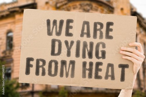 The phrase " We are dying from heat " on a banner in men's hand with blurred background. Global warming. Climate change. Ecosystem. Environment. Collapse. Temperature. Heat wave. Earth
