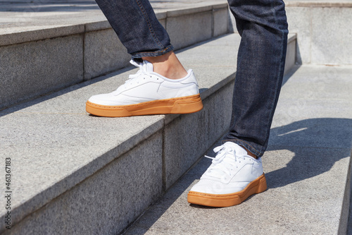 Male legs in jeans and white sneakers on background of concrete stairs.