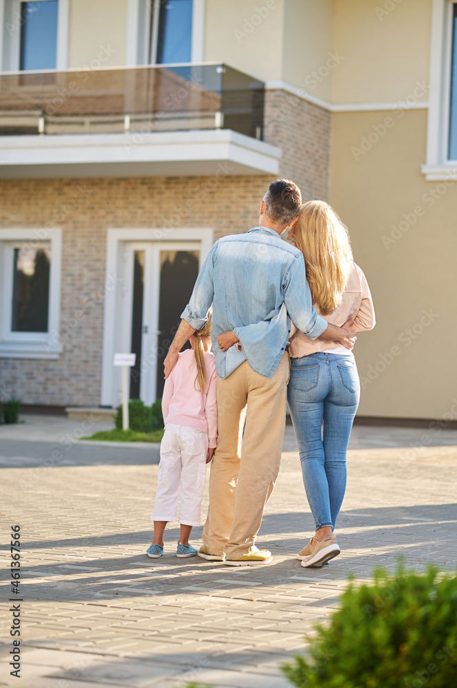 Man, woman and little girl hugging near house