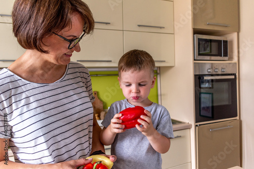 Adult woman is feeding her son sweet pepper. Vegetarian food. Communication of a mother with a child at home. photo