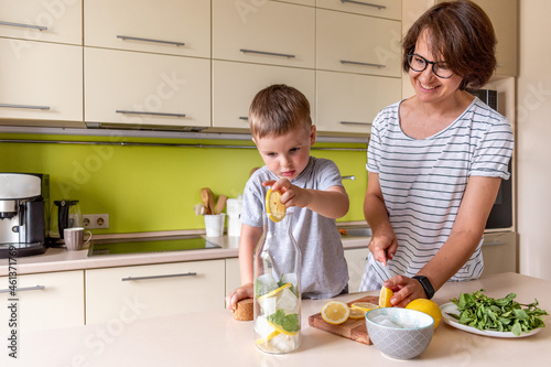 Adult woman is preparing lemonade with her son. Cold drink. Summer heat. Vegetarian food concept.