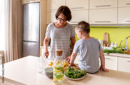 Adult woman is preparing lemonade with her son. Cold drink. Summer heat. Vegetarian food concept.