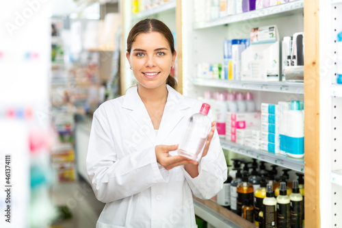 Portrait of a smiling young woman pharmacist in the sales hall of a pharmacy  demonstrating recently received goods for ..sale in hands