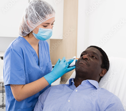 Adult african man patient of cosmetologist receiving hyaluronic acid injections in cosmetology clinic