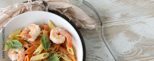 flat lay of a bowl of colorful pasta with shrimp and basil on a light wooden table