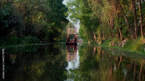 Traditional colorful trajinera surrounded by trees in Xochimilco lake photo