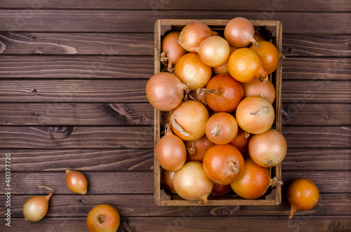 Large raw onions in a box on a wooden background.