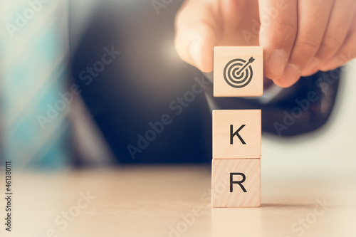 Business plan with OKR(Objectives and Key Results). Man holds wooden cube blocks with goal icon and OKR text. For developing business performance. Achieve business growth by flexible management.