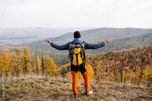 A man stands on a rock with his arms outstretpped and contemplates a magnificent view from the top of the autumn forest. Travel to the mountains, bright clothes, climbing, panoramic view.