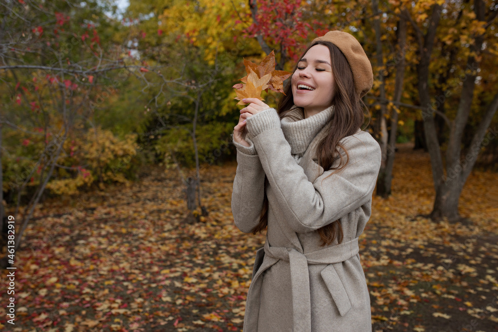 A young girl in a coat and beret stands in the park in the fall rejoices and holds maple leaves in her hand. A young girl in a coat and beret stands in the park in the fall rejoices and holds maple leaves in her hand.