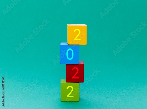 Colorful wooden building blocks with number 2022 stacking on green background