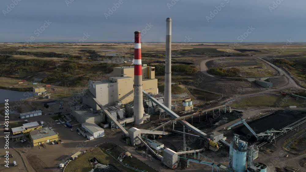 Aerial 8k hyperlapse circling Generating station in Canadian countryside during sunset underneath cloudy sky. Large powerplant with two high cooling towers fed by coal and gas.