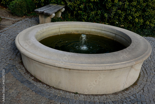 stone sandstone circular fountain in the park. built of sandstone filled with water. lined with a light threshing gravel road with a border of granite cubes, flowerbeds with orange flowers