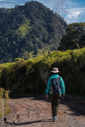 Hiker woman walking down a cobblestone path in rural area overlooking a beautiful green and mountainous landscape full of trees in Cartago Costa Rica