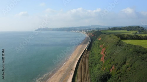 An aerial shot of a long train running along the South Devon coastal railway with the blue sea and seaside views heading towards Dawlish town on a sunny summers day photo
