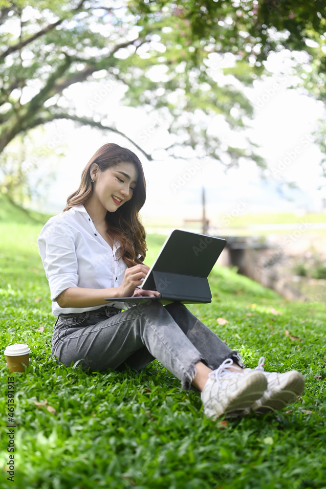 Young female freelancer sitting on grass in public park and working with computer tablet. Young female freelancer sitting on grass in public park and working with computer tablet.