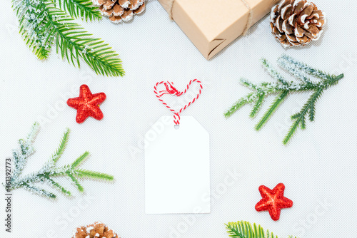 Christmas heart shape blank greeting card in frame of fir branches, decorations, gift box and cones over white background.mockup. flat lay. top view.
