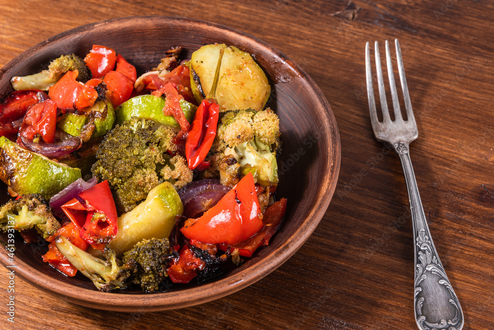 Baked vegetables - broccoli, zucchini, onions, tomatoes, peppers in a plate on a wooden table - rustic style Baked vegetables - broccoli, zucchini, onions, tomatoes, peppers in a plate on a wooden table - rustic style