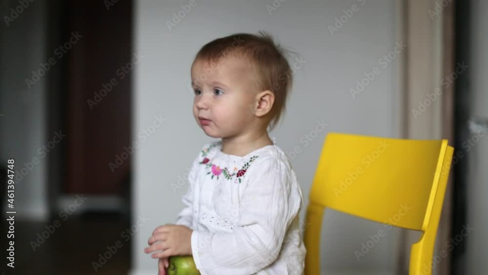 Cute caucasian child toddler eating green apple in kitchen in real interior Cute caucasian child toddler eating green apple in kitchen in real interior