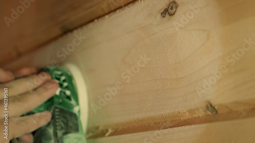 A hand with a grinding machine at the construction site. Male carpenter using a polishing machine for cleaning wooden log.