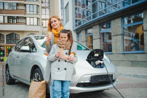 Stylish mother and daughter charge an electric car, and spend time together
