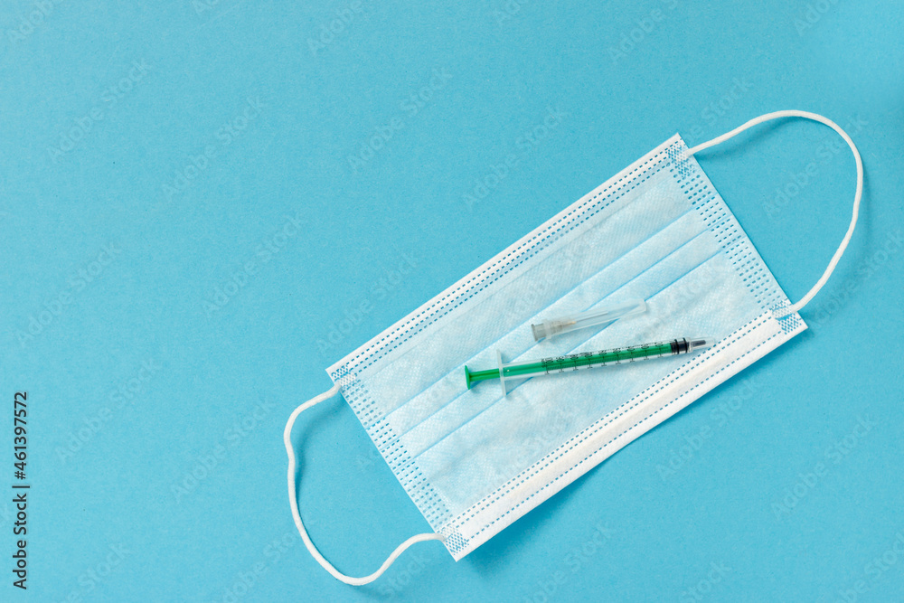 Medical mask and syringe on a blue background. Solid blue background with medical instruments. The concept of medicine, healthcare and science. Vaccine. Copy space for text. Medical mask and syringe on a blue background. Solid blue background with medical instruments. The concept of medicine, healthcare and science. Vaccine. Copy space for text.