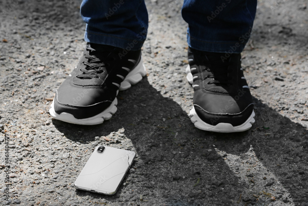 Legs of man and damaged mobile phone on pavement outdoors, closeup