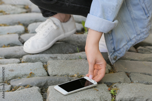 Woman picking damaged mobile phone from paving stones outdoors, closeup