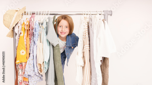 Shopping, kleines Mädchen schaut durch einen Kleiderständer fröhlich. Weißer Hintergrund Vs2