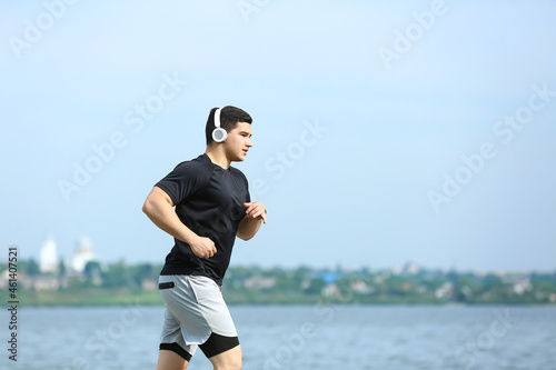 Fototapeta Naklejka Na Ścianę i Meble -  Muscular young man in headphones running near river