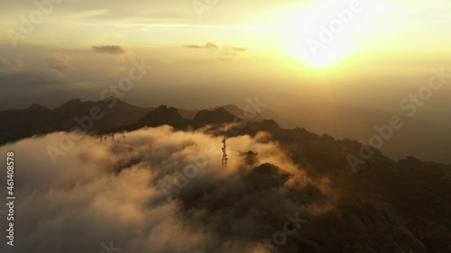 View from above, flying above the clouds, stunning aerial view of a mountain range with an antenna farm surrounded by clouds during a beautiful sunrise. Mount Limbara (Monte Limbara) Sardinia, Italy. photo