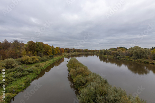 Autumn landscape with a river. Cloudy autumn day by the river. View of the river with trees and bushes on the bank. Bright colors of autumn on a cloudy day.