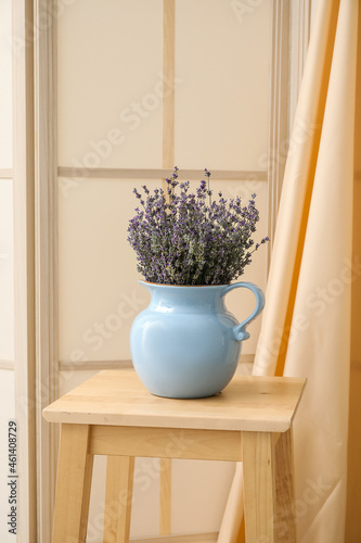 Jug with beautiful lavender flowers on chair in room
