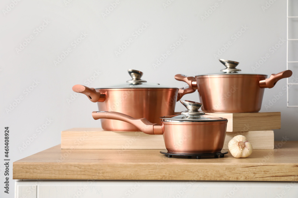 Set of copper cooking pots with garlic on counter near light wall Set of copper cooking pots with garlic on counter near light wall