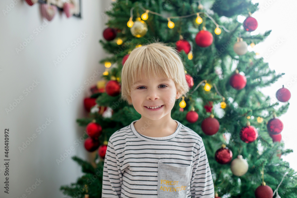 Beautiful toddler child, decorating   Christmas tree, presents under the trees