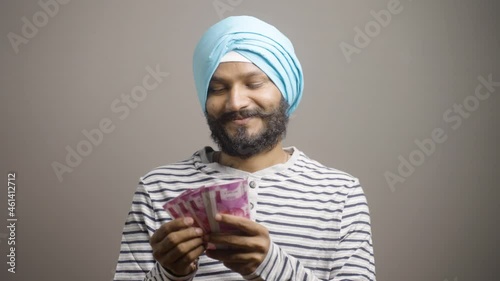 Happy smiling Indian sikh man counting Money on stuido background - concept of profit masking, won lottery, success ful young man photo