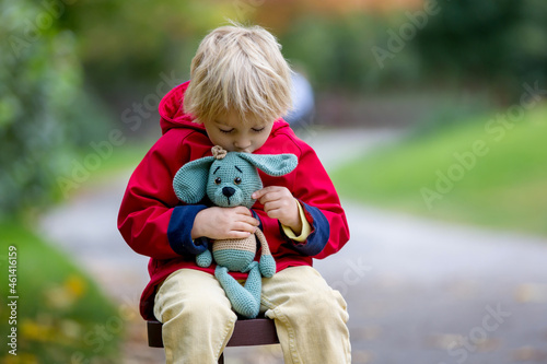 Little toddler child, boy, playing with knitted amigurumi dog toy in autumn park photo