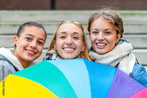 group of young girls demonstrating for the rights of the LGBT community, portrait of three women with the colors of the flag symbolizing tolerance and equality on an umbrella