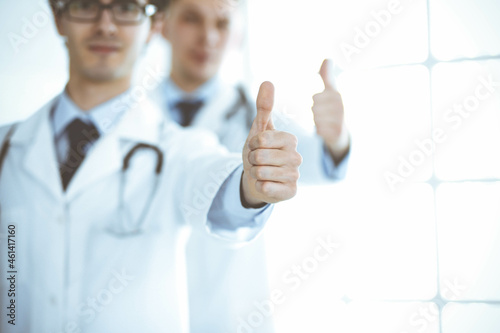 Two male doctors standing as a team and showing thumbs up as a symbol of the best service for patients in the clinic. Medicine and health care