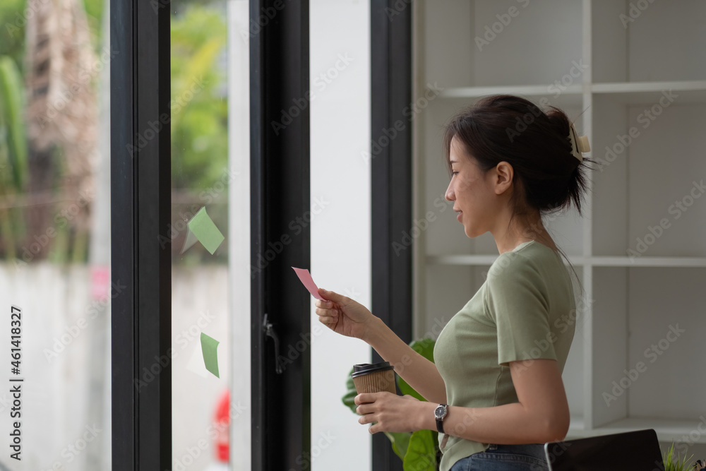 Creative business asian woman reading sticky notes on glass wall at office.